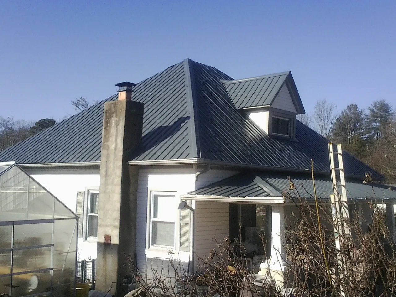 Dark blue standing seam metal roof on a white farmhouse with dormer — Slate & Tile Roof Repair by Roofing Brothers in Panora