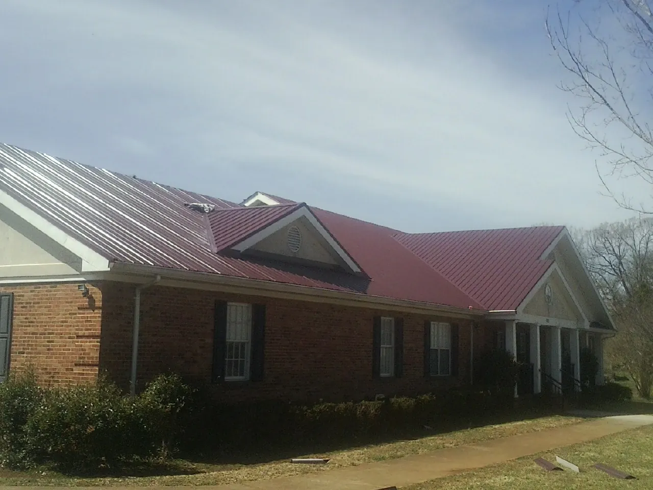 Red metal roof with gabled entries on a long brick building, from a Hail Damage Roof Repair job in Panora