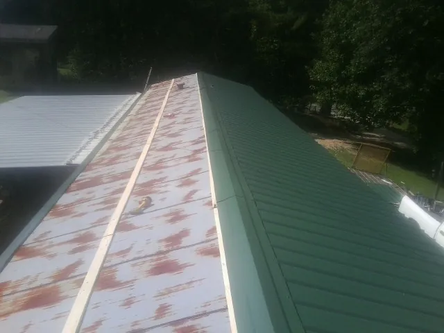 Old rusted panels beside newly installed green metal roofing — Wind Damage Roof Repair by Roofing Brothers in Panora