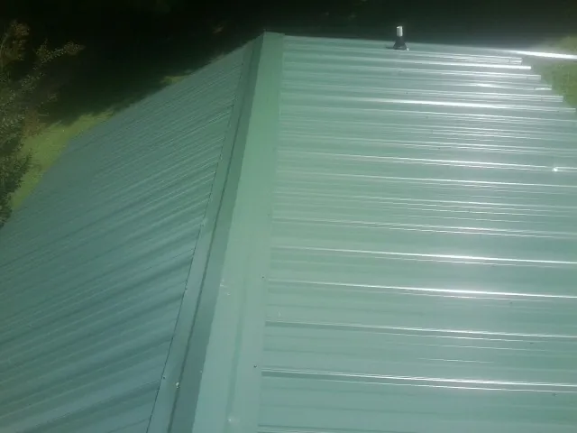 New green metal panels meeting at the ridge of a roof — Flat Roof Repair work by our crew in Panora