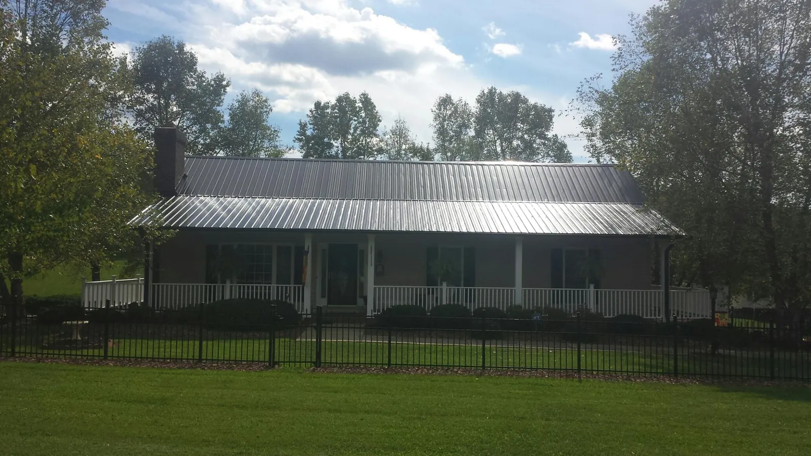 Gray metal roof on a brick ranch with a full width front porch — Gutter Guard Installation work by our crew in Panora
