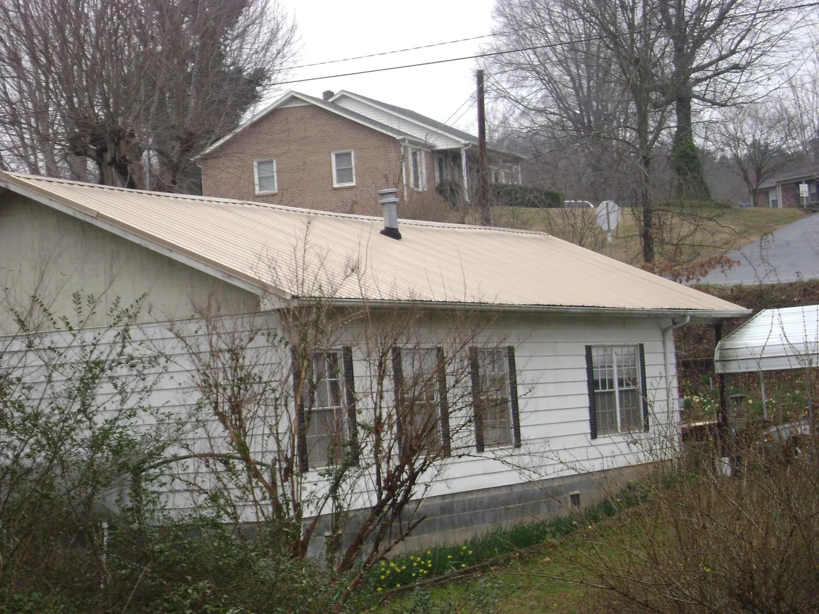 Tan metal roof on a white sided house set into a hillside — Commercial Roofing by Roofing Brothers in Panora
