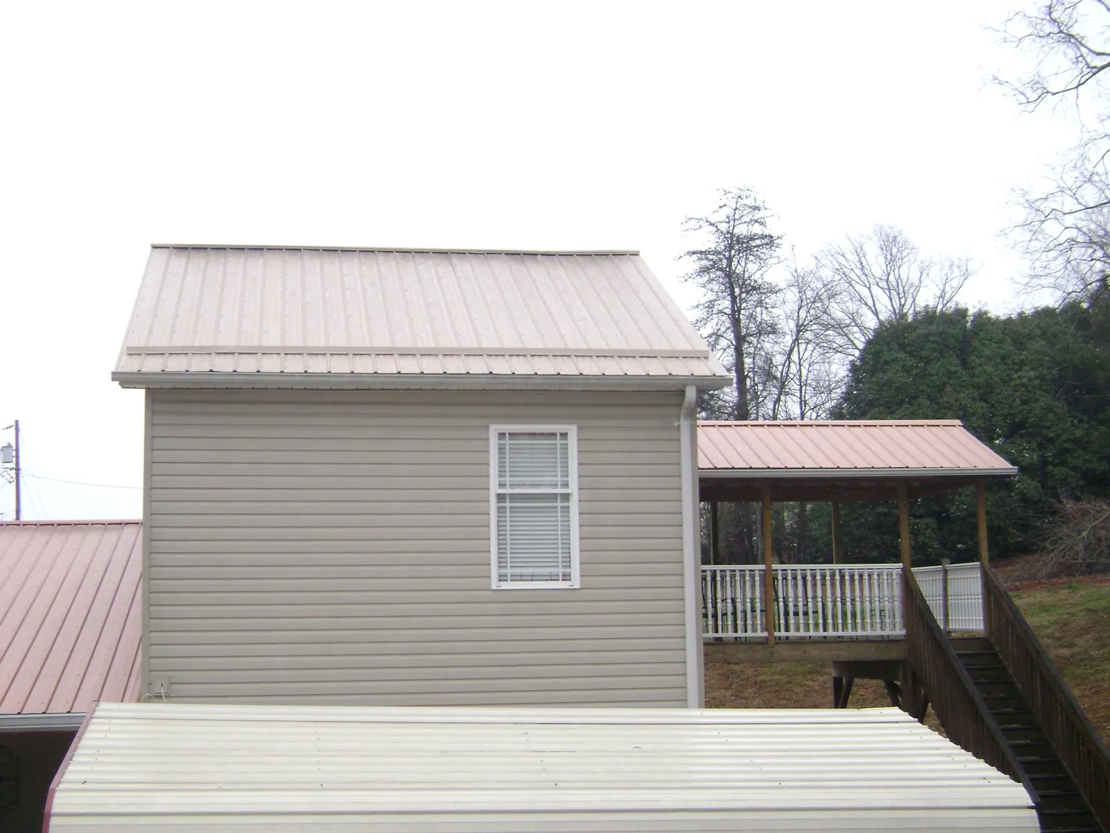 Tan metal roofs on a two story addition and attached porch, from a Roof Replacement job in Panora